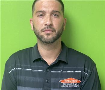 Male employee with brown hair hair and black SERVPRO shirt smiling in front of green background.