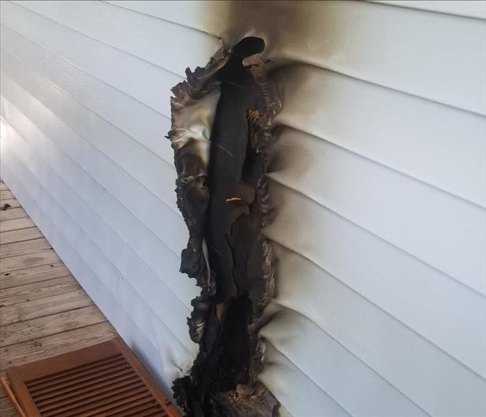 Siding burnt on the side of a home with a wood porch. 