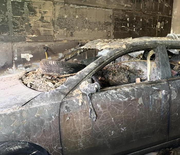 A burnt car with soot and fire damage with a tire on the dash. 
